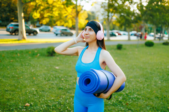 Fit female athlete holding a yoga mat in the sunny summer park.