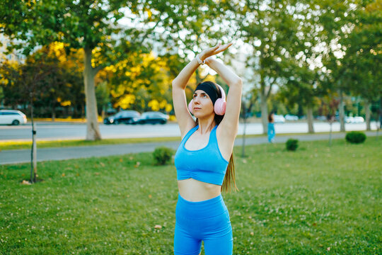 Active woman performing an arm stretch routine in the sunny summer park.