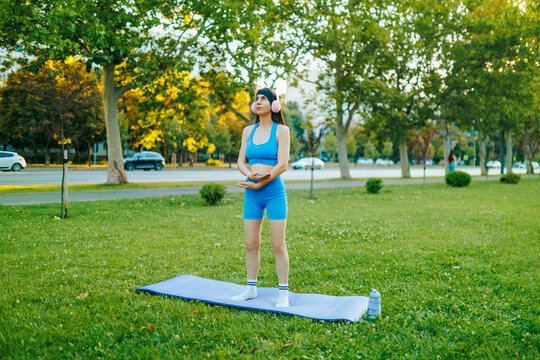 Athletic young girl standing on a yoga mat in the green city park.