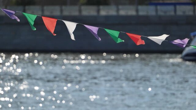 Colorful pennant banner strung over sparkling water with bokeh in bright sunlight