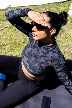 Woman in sunglasses resting on mat after outdoor workout