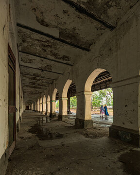 View of the historic Bahawalnagar Railway Station corridor with weathered arches, peeling paint, and people walking in the background in Bahawalnagar, Punjab, Pakistan.