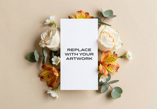 Vertical card mockup with replaceable artwork, surrounded by roses, orange alstroemeria, eucalyptus, and small flowers on a beige surface, stationery branding presentation, template