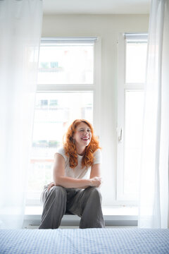 Smiling redhead woman sit by bright bedroom window