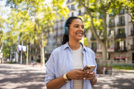 Smiling Hispanic woman with headphones and smartphone outdoors