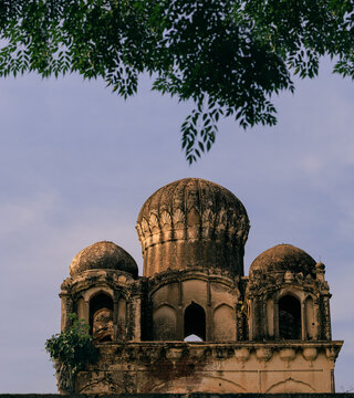View of the historic Guru Kotha with its ornate domes and arched openings, framed by foliage in Wazirabad, Punjab, Pakistan.