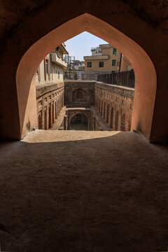 View of the historic Baahar wali Bawli stepwell framed by an arched entrance with weathered brick masonry and sunlight in Kharian, Punjab, Pakistan.