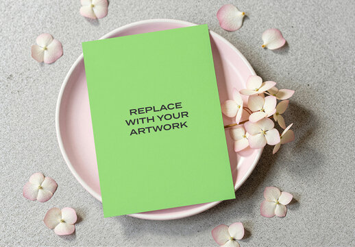 Vertical card mockup displayed on a pink plate with scattered hydrangea flowers textured gray surface, flat lay presentation natural lighting, design