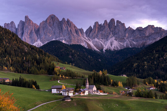 View of the Dolomites rising above the village with a historic church and green alpine meadows in Campitello di Fassa, Trentino-Alto Adige, Italy.