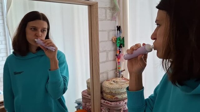 Woman brushing her teeth while looking in the mirror in a bright bathroom