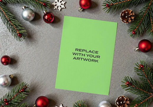 Vertical poster mockup displayed on a gray textured surface surrounded by Christmas decorations including pine branches, red and silver ornaments, snowflakes, pinecones