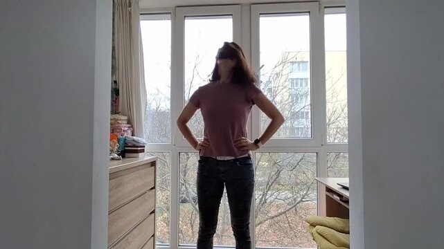 Woman stretches in her home by the window during afternoon in an urban area