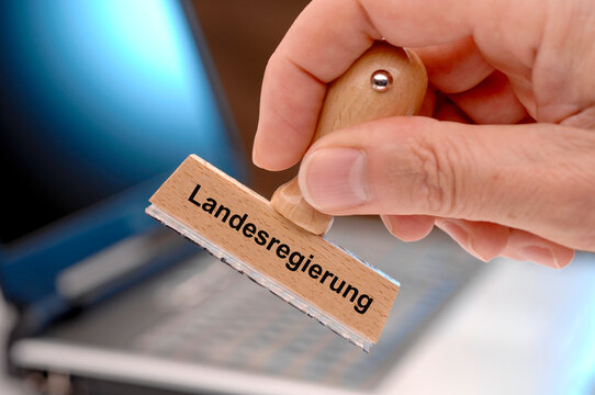 Eine Hand h&auml;lt einen Holzstempel mit dem Aufdruck: Landesregierung