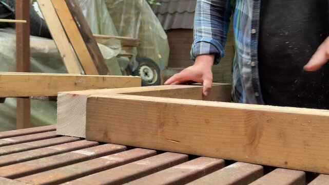 Close-up of a man handling wooden beams and assembling a timber structure outdoors. Hands-on woodworking and construction process during a DIY backyard improvement project in a natural garden setting.