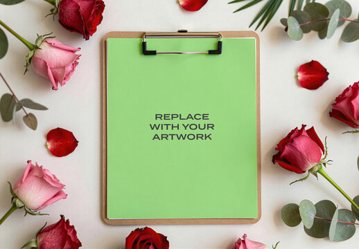 Stationery mockup featuring a clipboard with paper on white surface, surrounded by red and pink roses eucalyptus leaves in flat lay composition, design