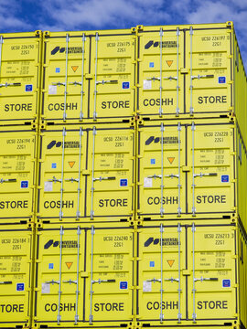 Yellow shipping containers. Marked with STORE and COSHH. Stand vertically stacked. Symbolizing efficient storage. Freight transportation. Global commerce