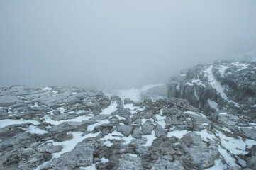 Fototapeta premium A wide horizontal shot of a rugged limestone mountain plateau covered with patches of snow and shrouded in thick fog in the Dachstein massif of Austria