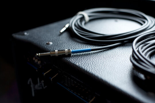 professional audio cable featuring a chrome-plated quarter-inch TS connector with a distinctive blue identification band, resting on a textured black leather amplifier case