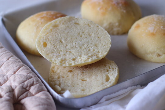 Homemade ciabatta bread rolls arranged on a parchment lined baking tray with sliced pieces revealing the soft, airy crumb. Rustic food styling highlights texture, freshness, and artisan baking