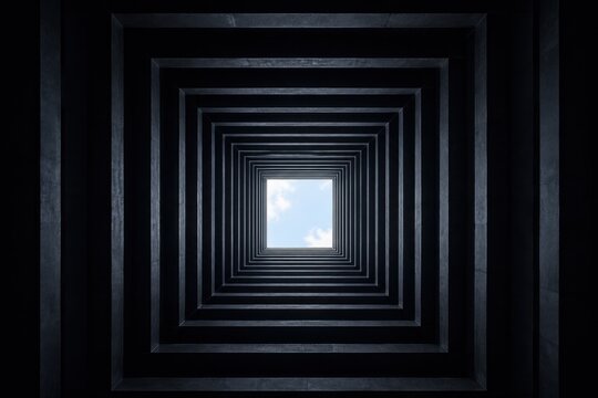 Looking up through a dark square tunnel towards the bright blue sky
