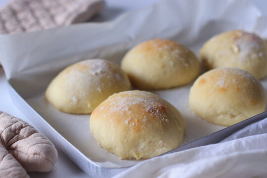 Freshly baked ciabatta bread rolls displayed on a metal baking tray lined with parchment paper. Soft texture, golden crust, and a minimalist homemade presentation create an inviting bakery scene