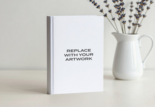 Hardcover book mockup with placeholder text displayed on a light surface in minimalist interior setting, featuring ceramic pitcher holding dried lavender, Template