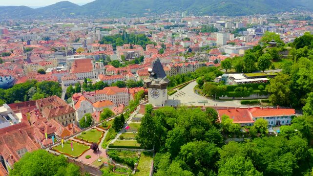 Graz, Austria. The Uhrturm clock tower with reversed hands and wooden gallery, Drone footage over terracotta rooftops and the historic city center. Drone footage, Departure of the camera