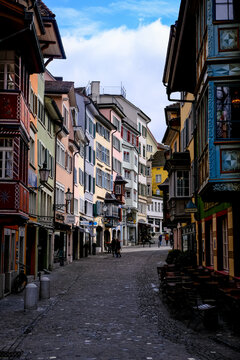 Zurich, Switzerland - March 15, 2026. Colorful Historic Buildings and Oriel Windows on Augustinergasse in Zurich Old Town. A low-angle, vertical eye-level shot captures the vibrant charm of Augustiner