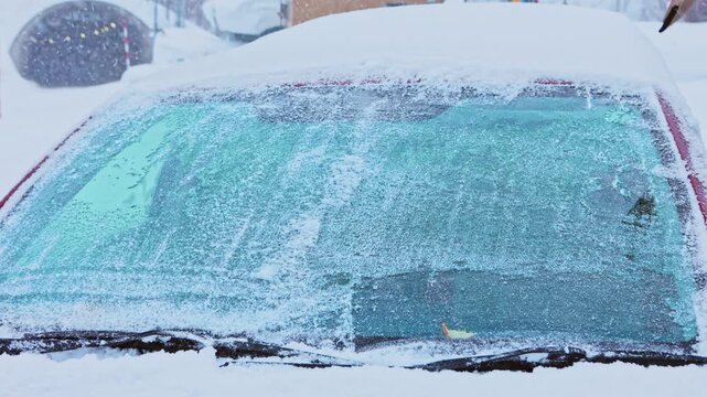 Driver cleaning snow and ice from a car windshield