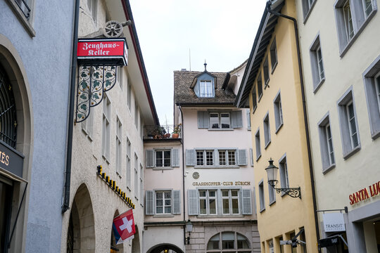 Zurich, Switzerland - March 15, 2026. Historic Narrow Street with Zeughauskeller and Grasshopper Club Building in Zurich. A low-angle shot highlights a charming, narrow cobblestone alley in the histor
