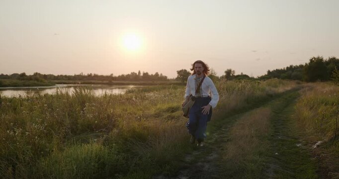 Caucasian man with long hair and Ukrainian traditional folk attire run away being chased . 4K 10-bit