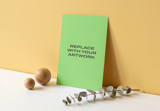 Vertical poster mockup displayed on a white surface against textured yellow wall, realistic print presentation with wooden spheres and eucalyptus branch, Template