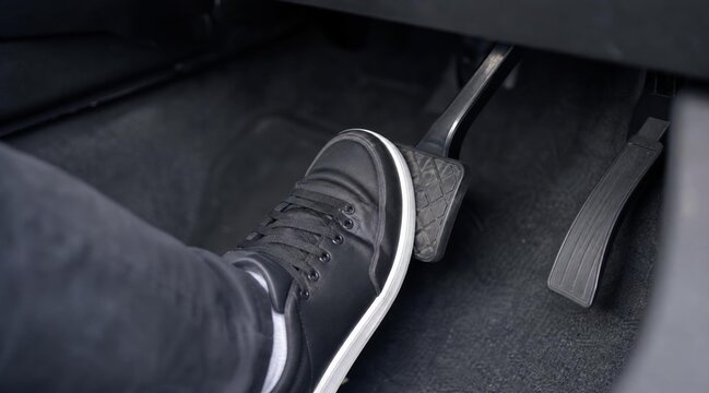 Person pressing the brake pedal in a car with a black sneaker.