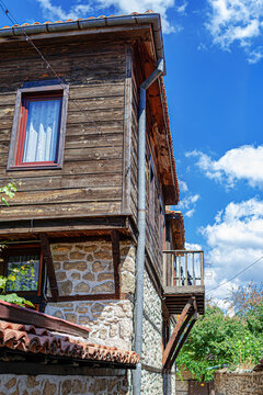 An old traditional wooden and stone house stands against a bright blue sky with white clouds.