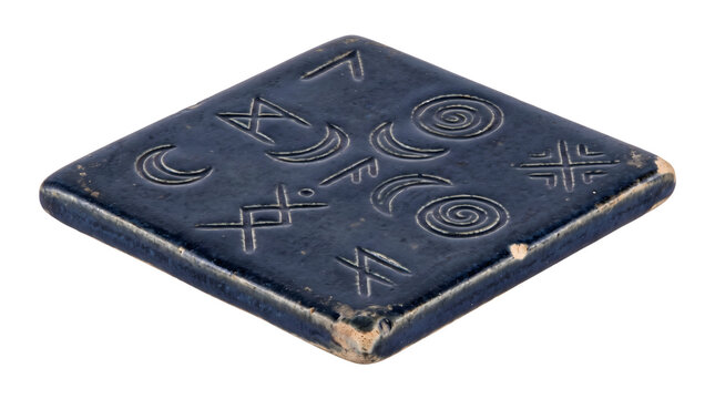 Ancient dark blue ceramic tile with carved mystic symbols and runes spiritual pagan ornament isolated on background.