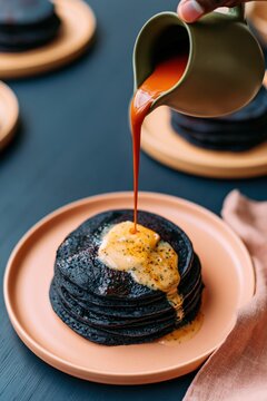 Vertical portrait of black pancake stack with butter and caramel sauce being poured over for breakfast menu or poster background