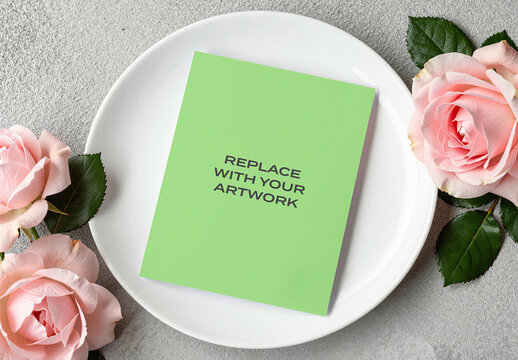 Card mockup on a white plate with pink roses in flat lay composition, stationery branding presentation, floral arrangement, interior setting, product display, graphic design template
