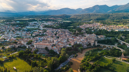 Fototapeta premium Aerial panoramic view of Besalu medieval town and historic stone bridge in Catalonia Spain surrounded by mountains and green countryside at sunset
