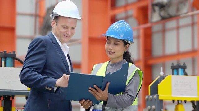 Two industrial engineers in safety helmets and protective vests review data on a tablet during a factory audit, supporting quality control, workplace safety, and business operations.