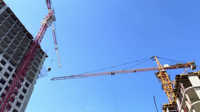 Multiple construction cranes move above unfinished towers against clear blue sky