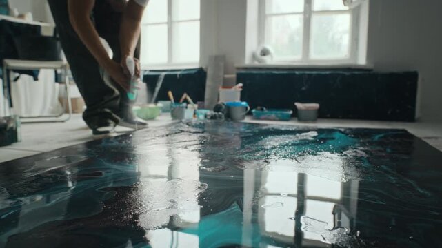 Young adult Caucasian male artist spraying water on fluid epoxy resin painting in studio, tilt up shot. Clip is ideal for creative industry promotions and art school advertisements