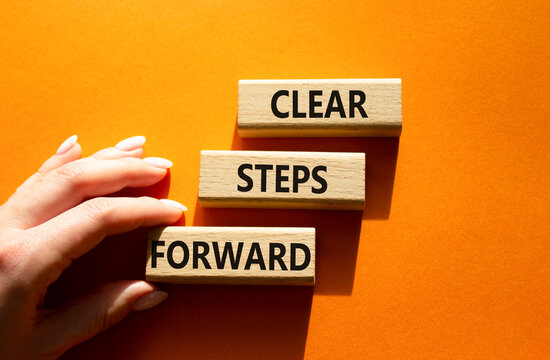Concept words clear steps forward on wooden blocks arranged as steps. Businessman hand arranging wooden blocks. Progress and planning concept. Orange background. Copy space.