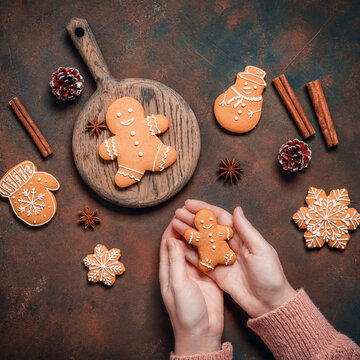 Gingerbread man in female hands on dark rustic background with Christmas decorations, top view, flat lay