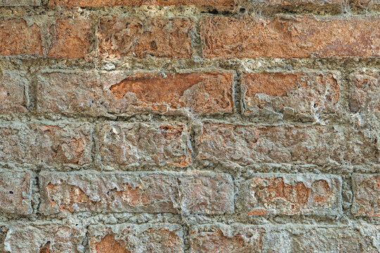 Weathered aged brick wall texture with faint cobwebs and eroded mortar between reddish stones