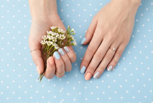 Elegant Female Hands with Pastel Blue and Peach Manicure Holding White Flowers over Polka Dot Background