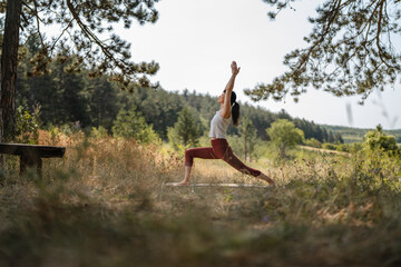 Fototapeta premium Woman practicing yoga warrior pose in nature