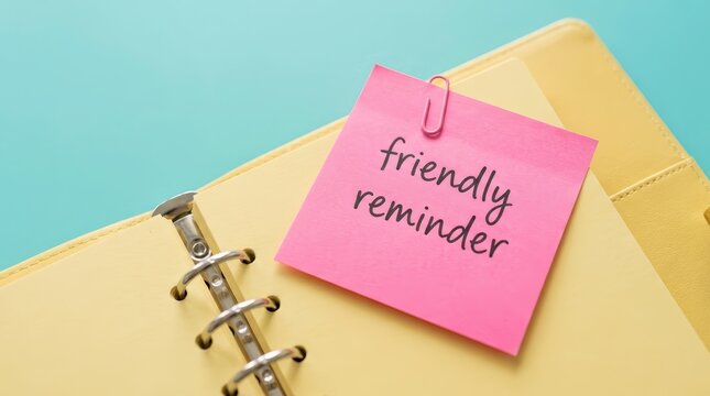 Friendly reminder message written on a pink sticky note attached to a yellow planner.