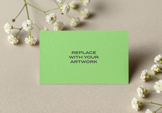 Textured business card mockup on a beige fabric surface with white baby's breath flowers, flat lay stationery presentation for print media, branding, Template, and advertising display