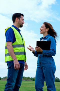 Vertical shot of Caucasian middle aged man in safety vest and Caucasian businesswoman discussing outdoor site plans with clipboard. Useful for construction management, inspection, teamwork