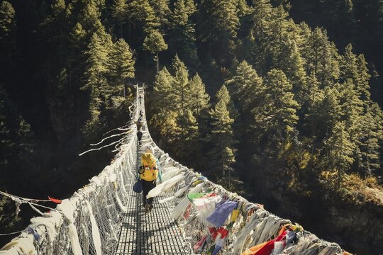 Caucasian woman trekking on famous bridge In Nepal outdoors surrounded by autumn nature. Chilly morning and travel outdoors in fall
